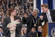 Holding my two-week-old baby at graduation, I watched my ex grab the microphone and shout, “Look at this pathetic dropout!” Five hundred guests laughed. I stood frozen until the university president interrupted. “She’s our valedictorian—and the sole heir to the $20 million trust funding this university!”